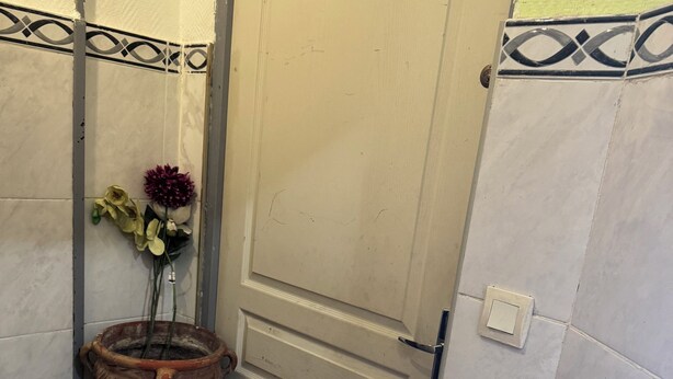 Ein Zimmer mit einer Tür, einem kleinen Podest mit einer Blumenvase und einem Fliesenboden.