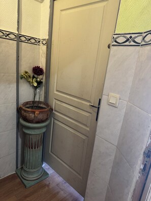 Una stanza con una porta, un piccolo piedistallo con un vaso di fiori e un pavimento piastrellato.