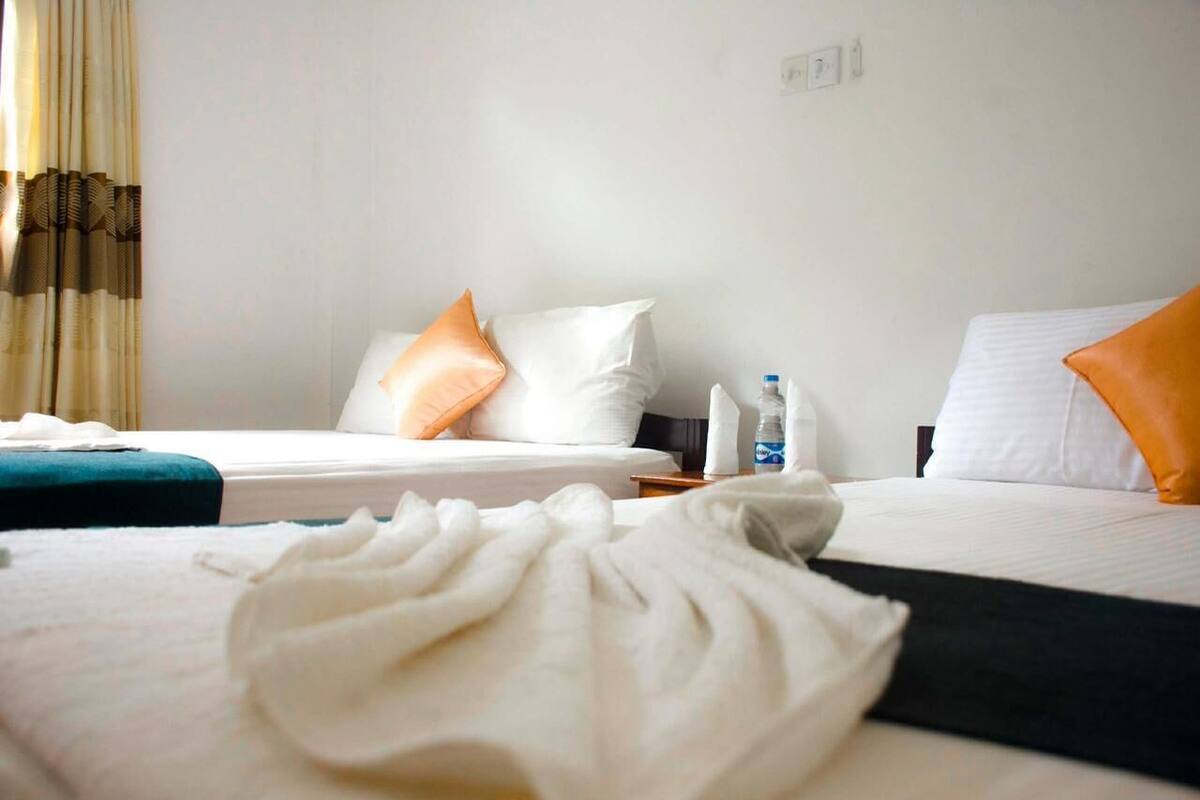 Ein Hotelzimmer mit zwei Betten, weißer Bettwäsche und orangefarbenen Kissen.