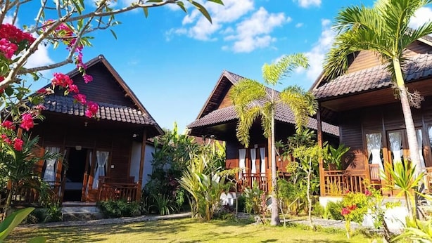A row of wooden cabins with tiled roofs, surrounded by lush greenery and flowering plants. - Kurnia Guest House and Spa (Penida Island)