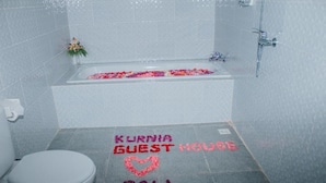 A bathroom with a bathtub, toilet, and a shower. The floor has text that reads "Kurnia Guest House Bali" and a heart shape. - Kurnia Guest House and Spa (Penida Island)