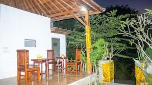 A covered outdoor area with wooden furniture and a white building in the background. - Kurnia Guest House and Spa (Penida Island)