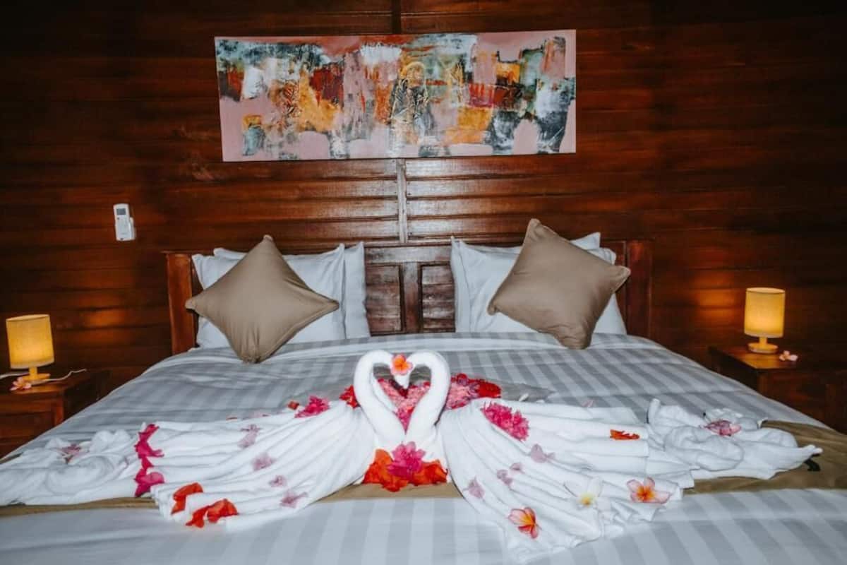Una habitación de hotel con una cama, cabecera de madera, dos mesitas de noche y un cuadro en la pared.
