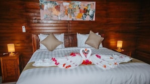A hotel room with a wooden headboard, two bedside tables with lamps, a bed with a white bedspread, and a decorative arrangement of towels and flowers on the bed. - Kurnia Guest House and Spa (Penida Island)