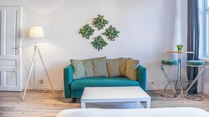 Una sala de estar moderna con un sofá color turquesa, una mesa de centro blanca, una lámpara de pie y un adorno de pared.