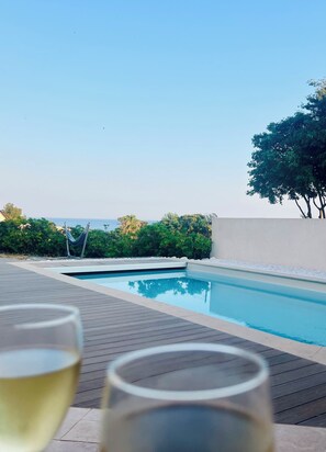 Ein Schwimmbecken mit freiem Blick auf das Meer, umgeben von Grünflächen und einer Holzterrasse.