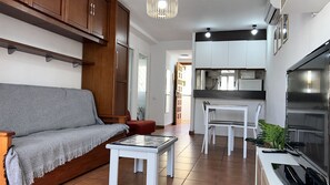 Een woonkamer met een bank, een kleine tafel, en een keukenhoek met een eettafel en stoelen.