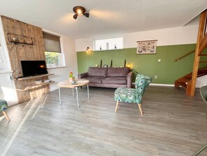 A living room with a wooden TV stand, a sofa, a round coffee table, and a peacock-patterned chair. - Charming Beachside Base in Noordwijk (Noordwijk)