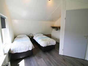 Een kamer met twee eenpersoonsbedden, een klein tafeltje en een witte deur.
