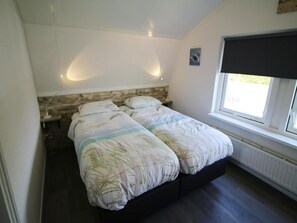 A bedroom with a double bed, a nightstand, a wall-mounted lamp, and a window with a view. - Charming Beachside Base in Noordwijk (Noordwijk)