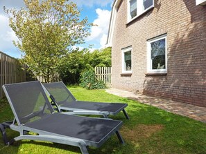 Een achtertuin met twee lounge stoelen, een bakstenen huis en een houten omheining.