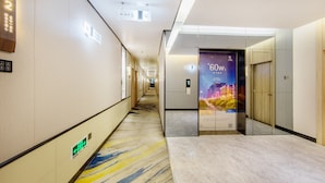 A hotel corridor with a patterned floor, directional signs, and an elevator with a cityscape advertisement.