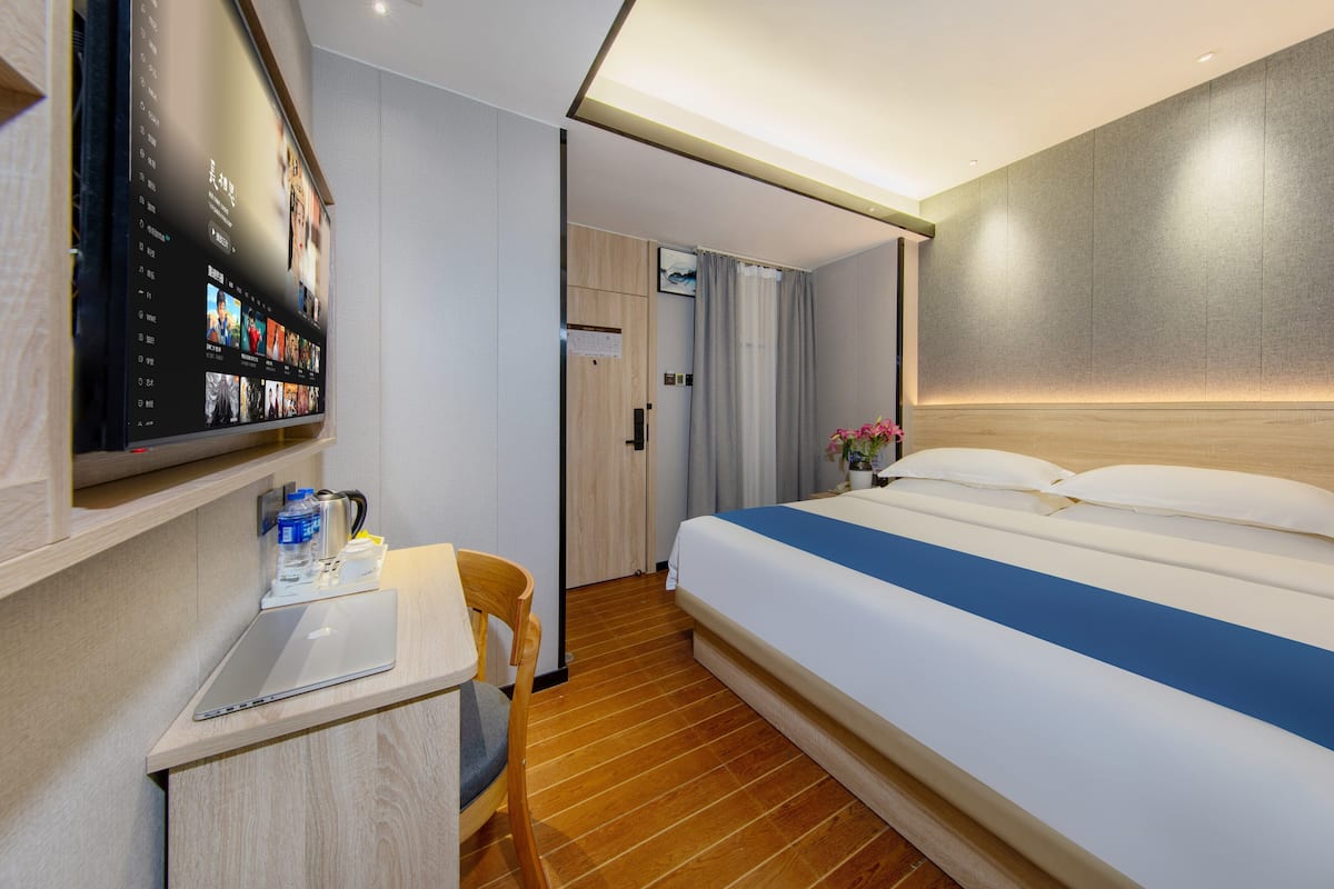 Habitación de hotel moderna con una cama grande, un escritorio con una computadora portátil y un televisor de pantalla plana montado en la pared.