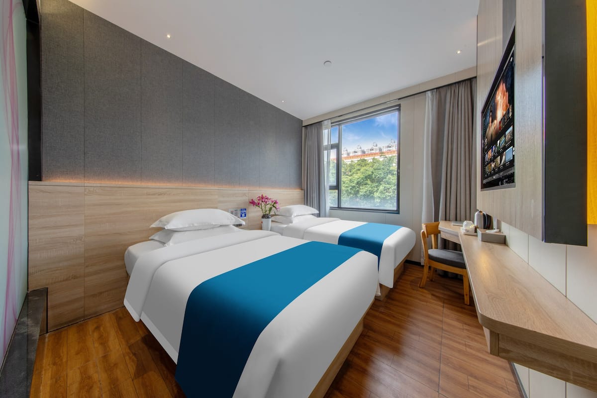 Habitación de hotel con dos camas, un escritorio, una silla, un televisor y una ventana con vista a la ciudad.