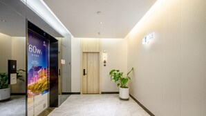 A modern hotel lobby with a marble floor, a wooden door, a potted plant, and a digital elevator display.