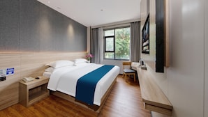 A modern hotel room with a large bed, wooden flooring, a desk, and a TV mounted on the wall.