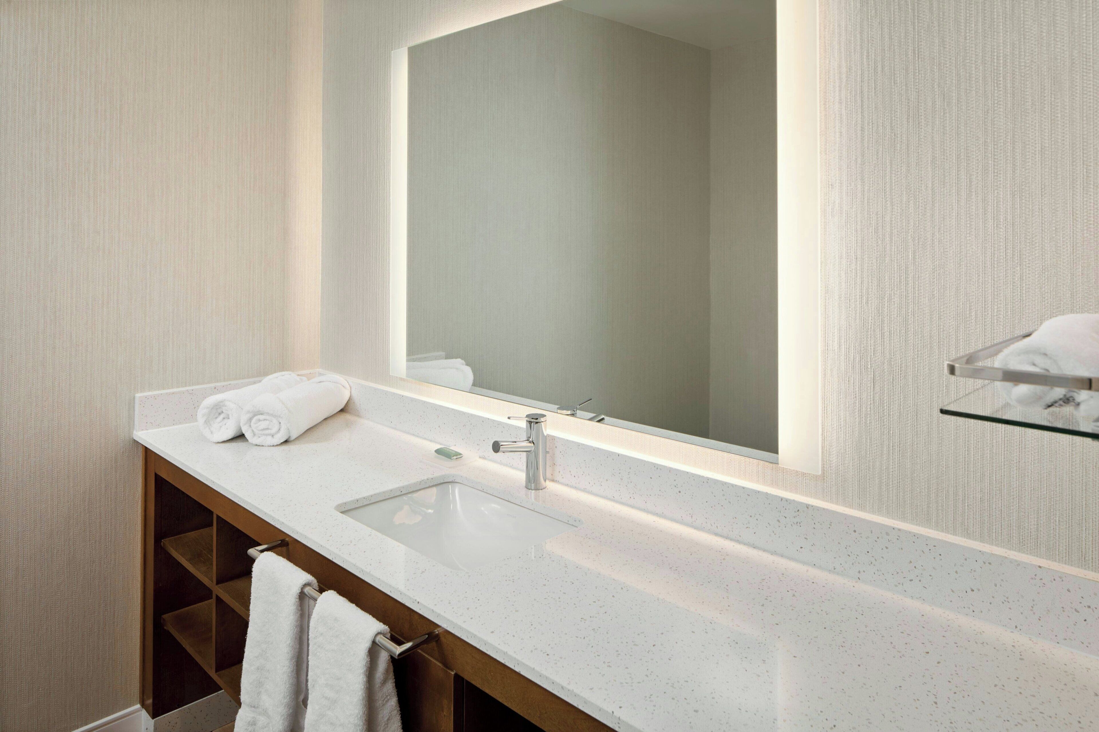Une salle de bain moderne avec un grand miroir, un lavabo blanc et un porte-serviettes.