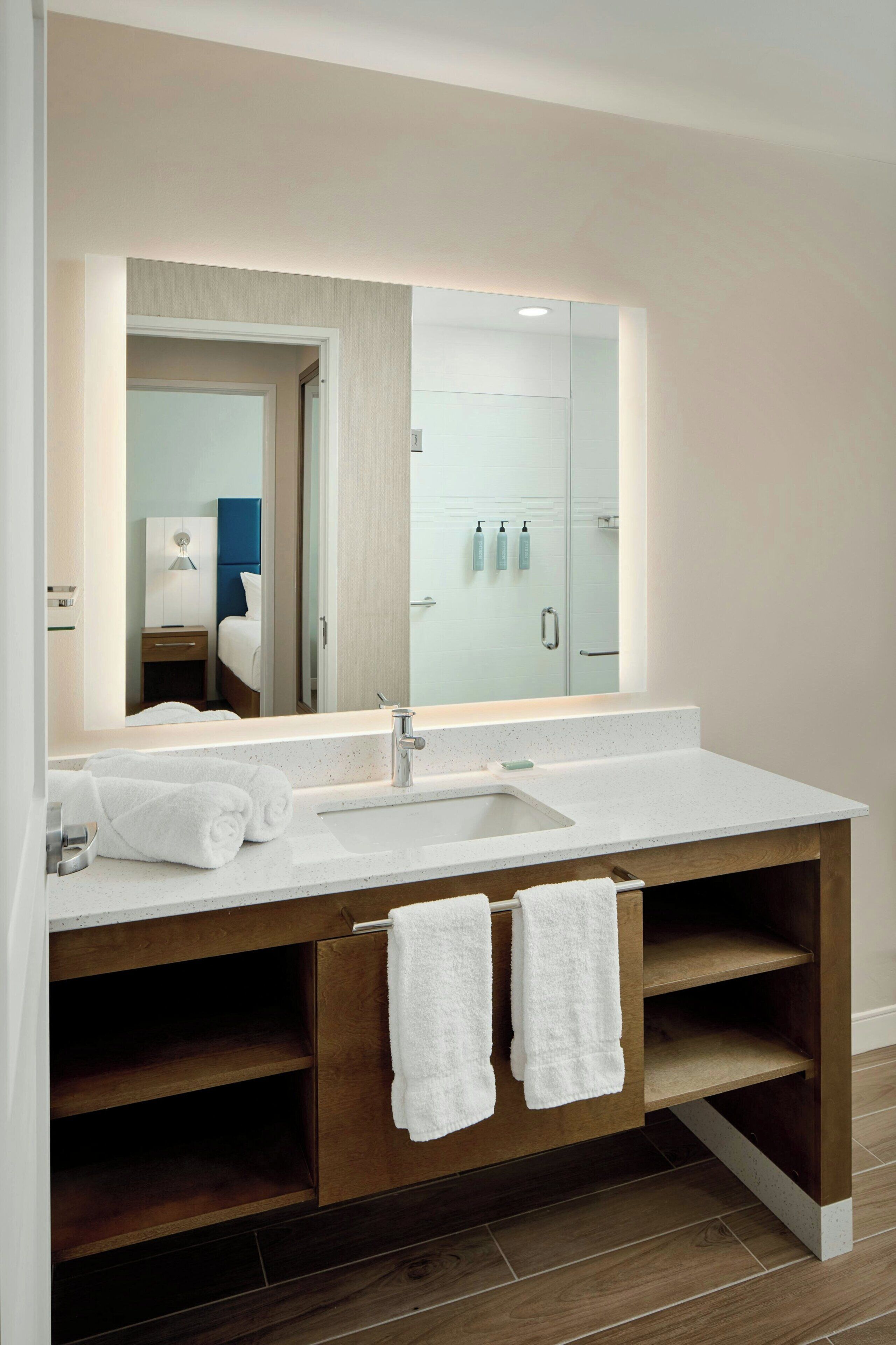 A modern bathroom with a large mirror, a white sink, and wooden vanity drawers.
