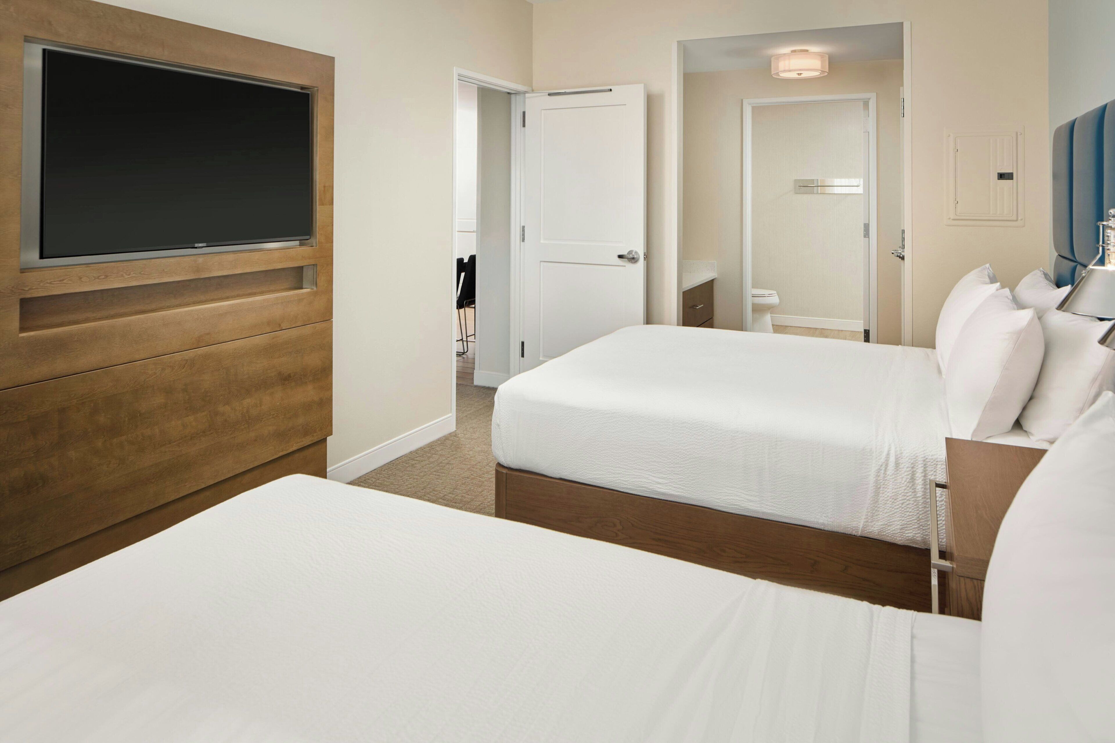 Camera d'albergo con due letti, una televisione fissata al muro, una porta e un bagno piccolo.