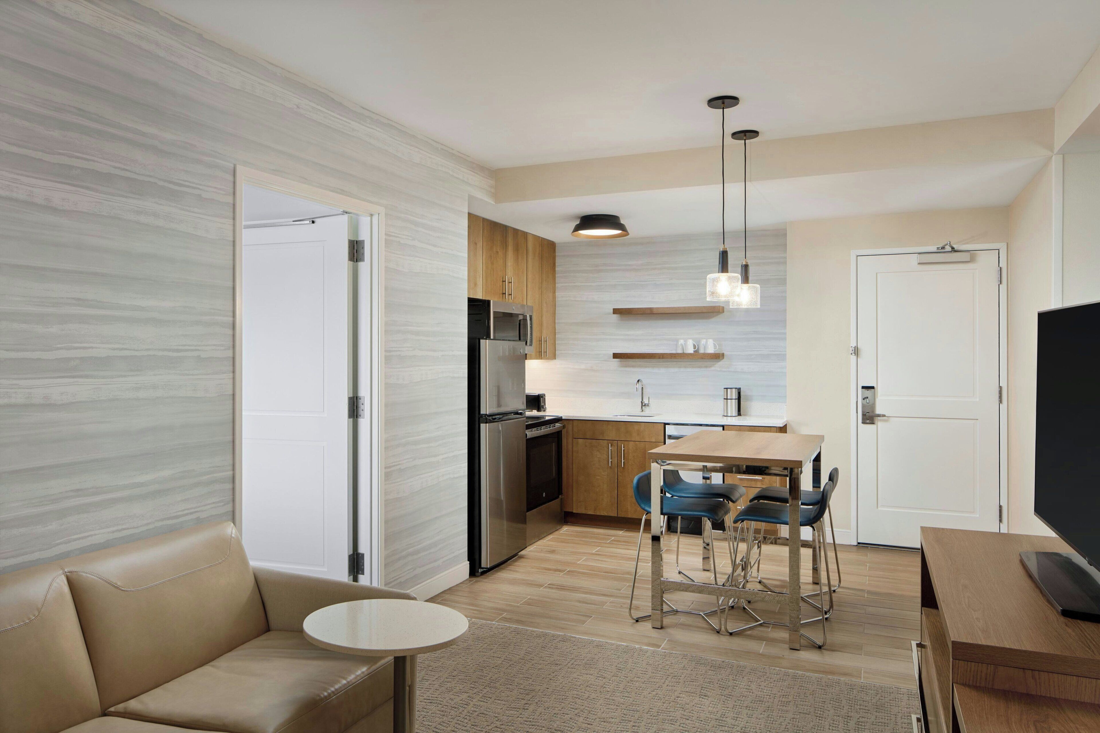 Una cocina moderna con refrigerador, microondas y estufa, un comedor con mesa y sillas, y una sala de estar con sofá y televisor.
