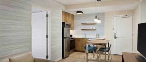 Una cocina moderna con refrigerador, microondas y estufa, un comedor con mesa y sillas, y una sala de estar con sofá y televisor.