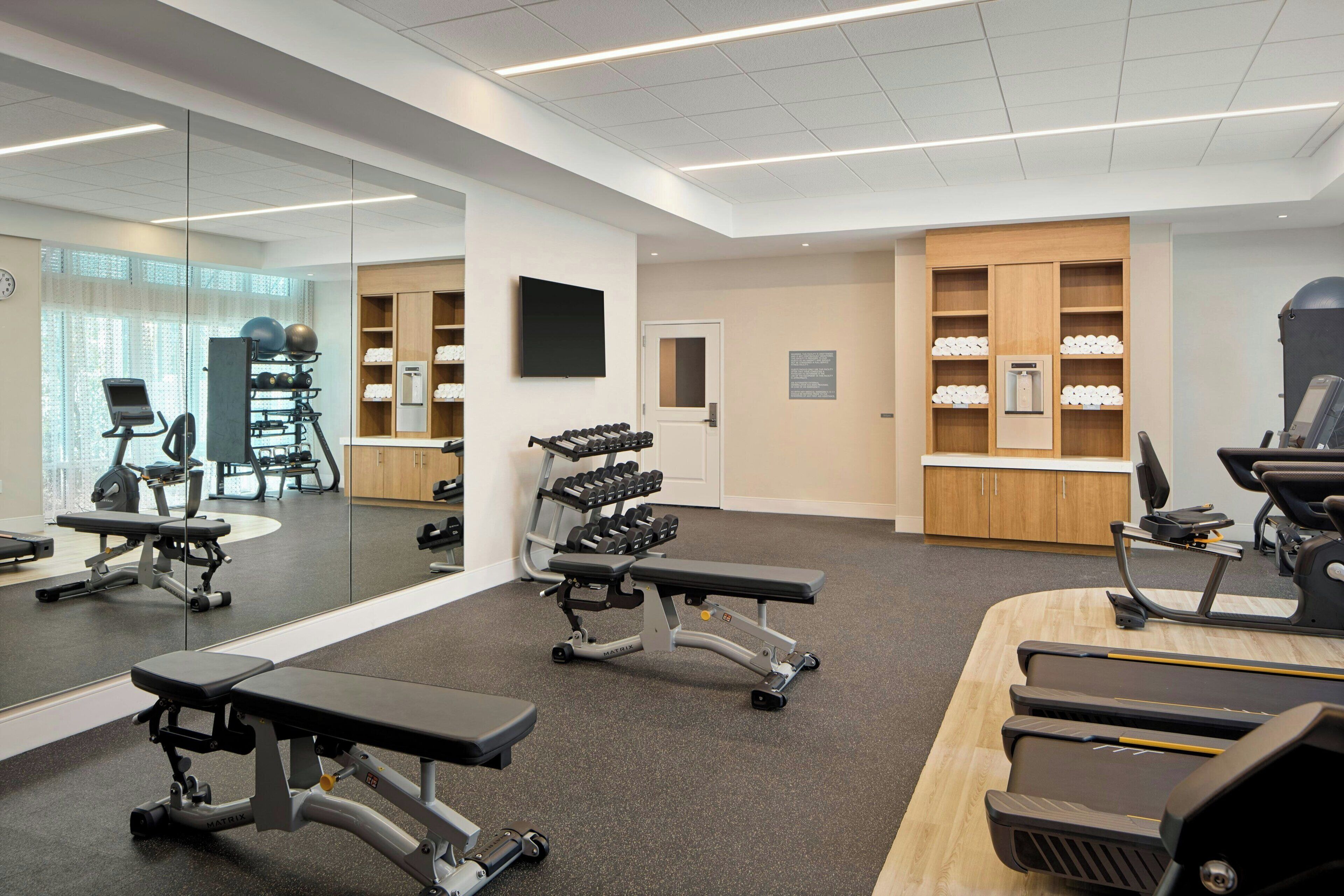 A gym with exercise equipment, a mirror, and a wooden cabinet with towels.