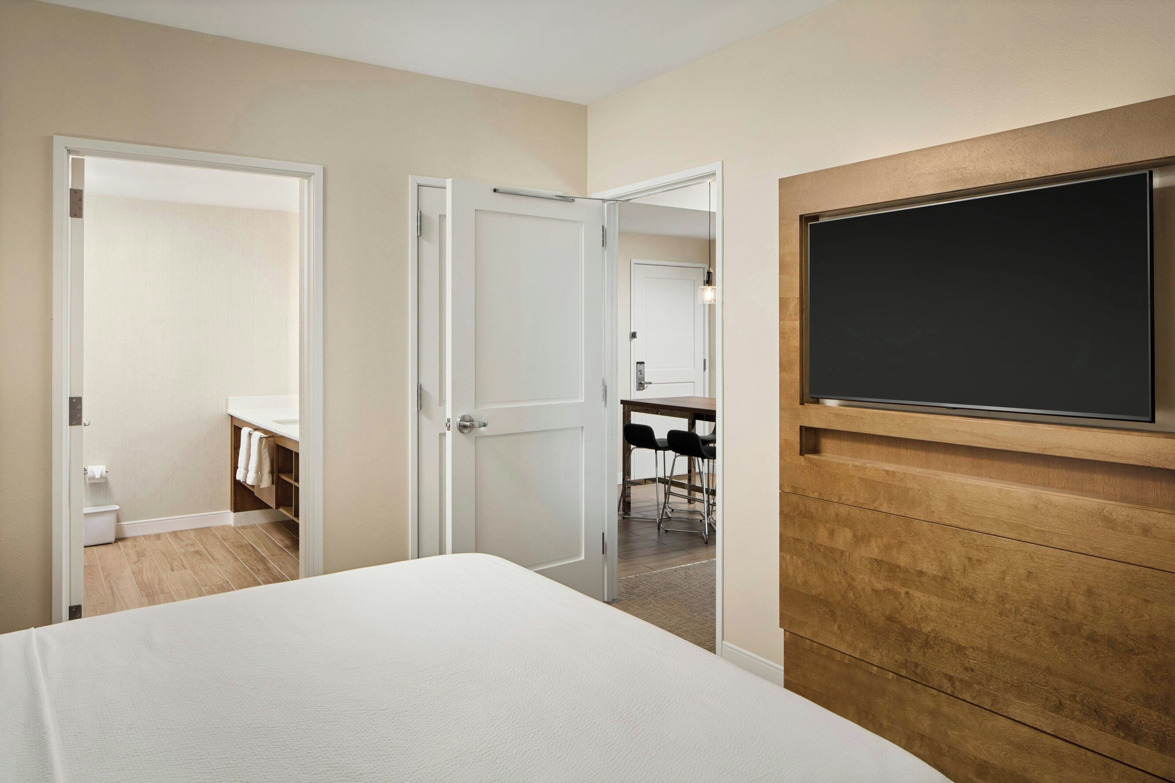 A bedroom with a bed, a TV mounted on the wall, and a bathroom visible through an open door.