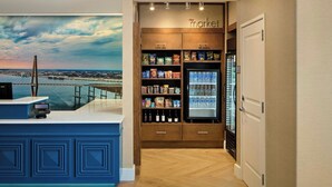 Eine Hotelhalle mit einer Rezeption, einer Minibar, einem mit Getränken gefüllten Kühlschrank und Blick auf eine Brücke.