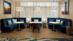 Ein modernes Wohnzimmer mit einer blauen Sofagarnitur, einem runden Tisch und einem großen Fenster mit gemusterten Vorhängen.