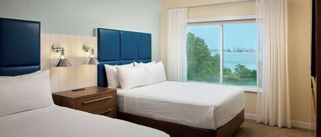 A hotel room with two beds, a nightstand, a lamp, and a window with a view of a body of water.
