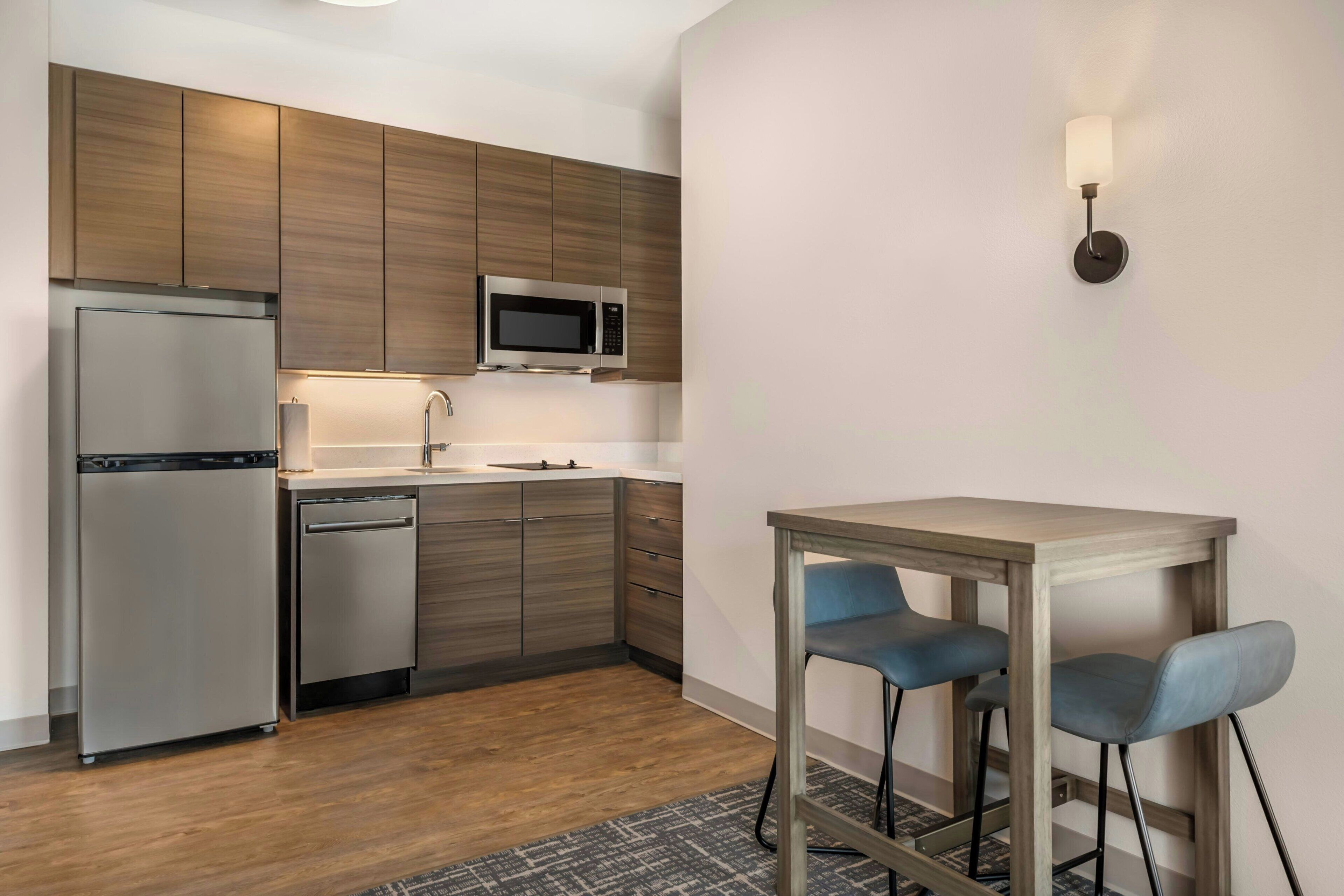 A modern kitchen with a refrigerator, microwave, and sink, and a small dining area with two chairs.