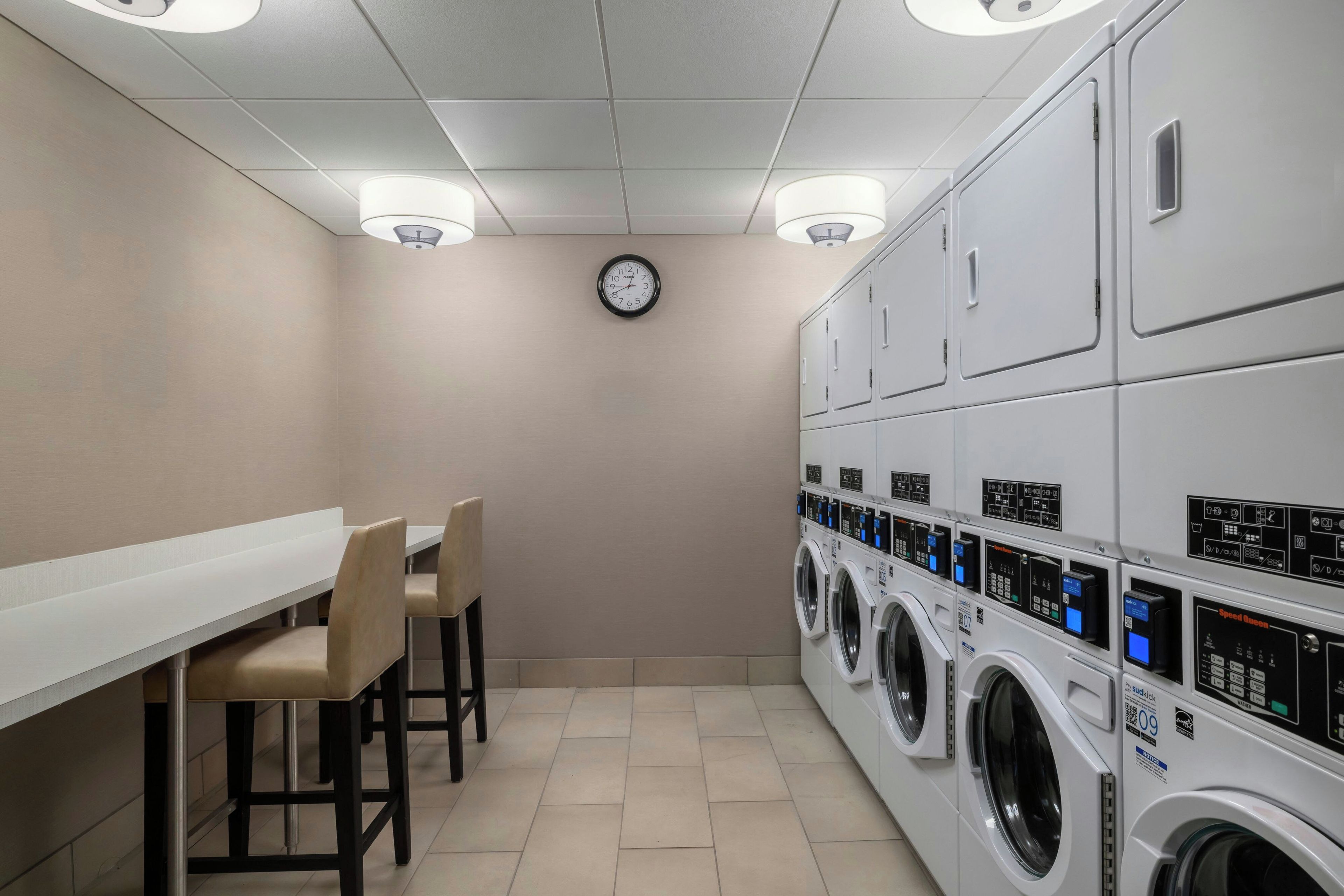 A laundry room with a long bench, chairs, and stacked washing machines.