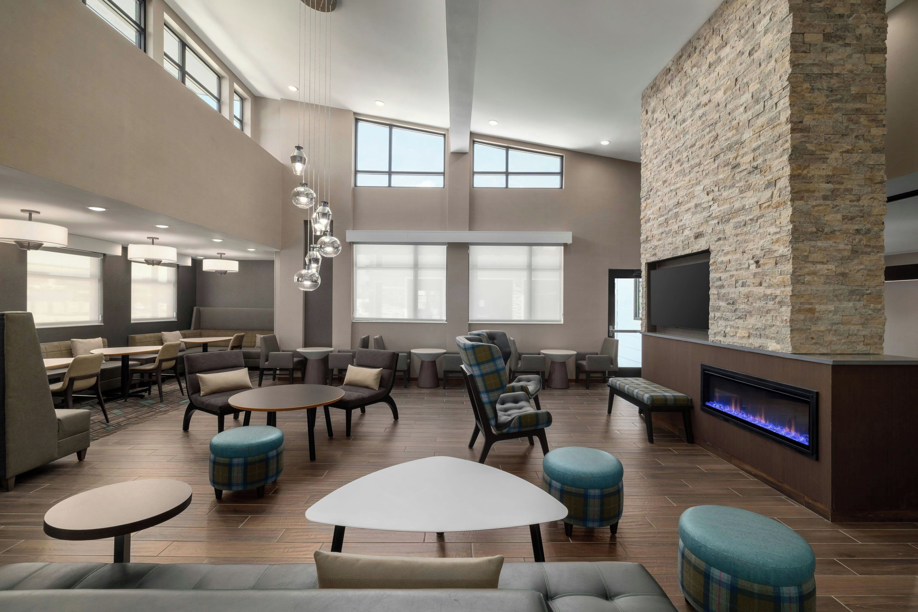 A spacious indoor area with multiple seating arrangements, including sofas, chairs, and tables. There is a fireplace with a modern design, and the space is well-lit with natural light from large windows.