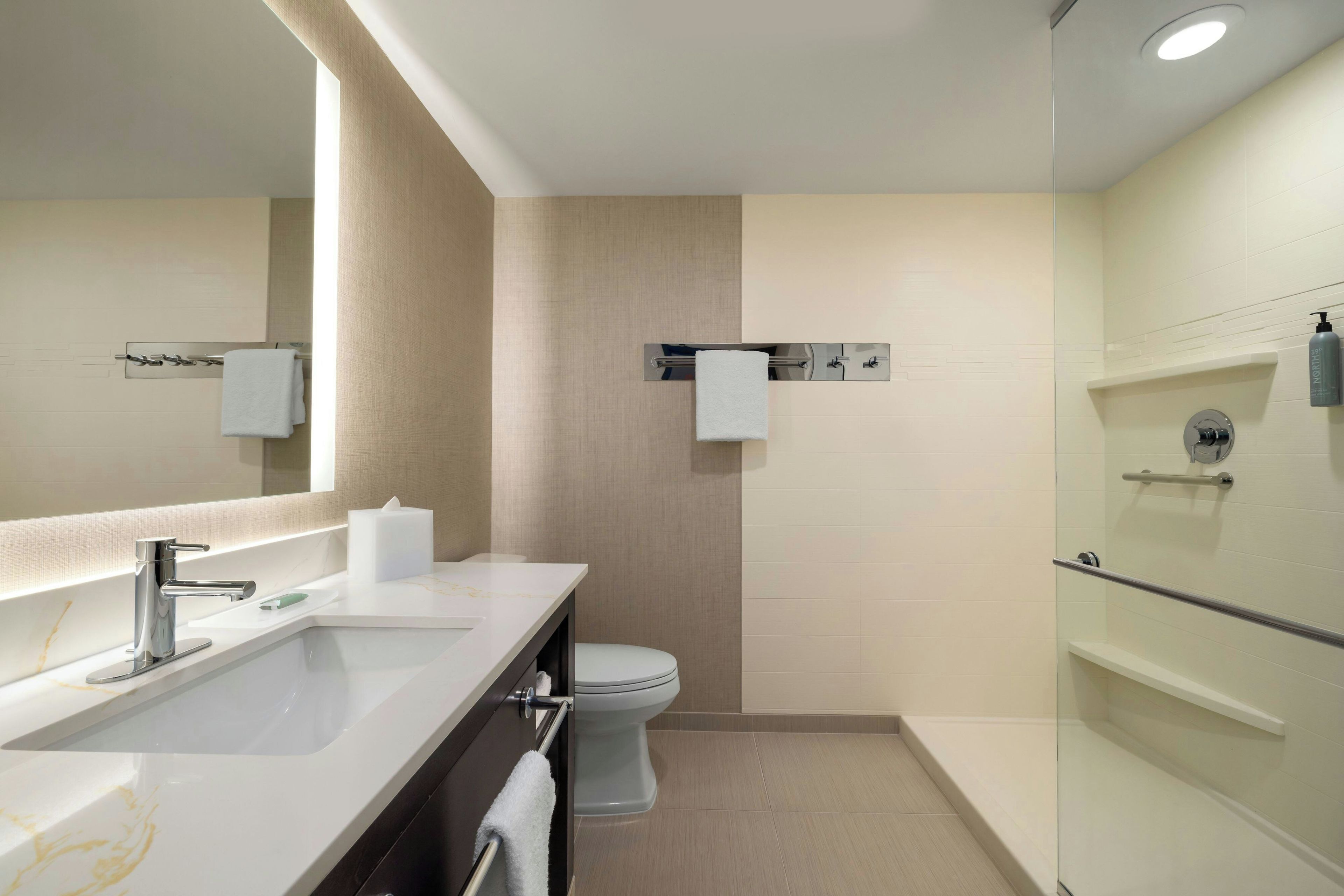 A modern bathroom with a large mirror, a sink, a toilet, and a glass-enclosed shower area.