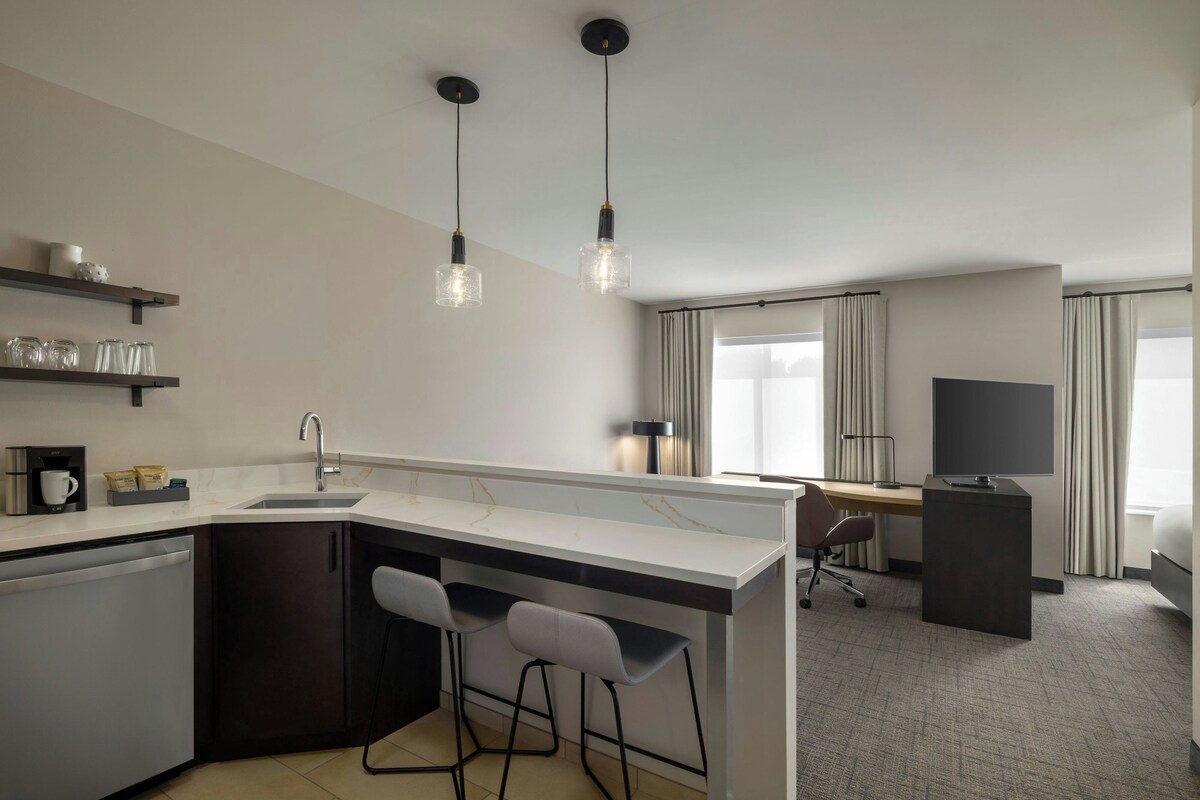 A modern kitchen with a central island, bar stools, a coffee machine, and pendant lighting.