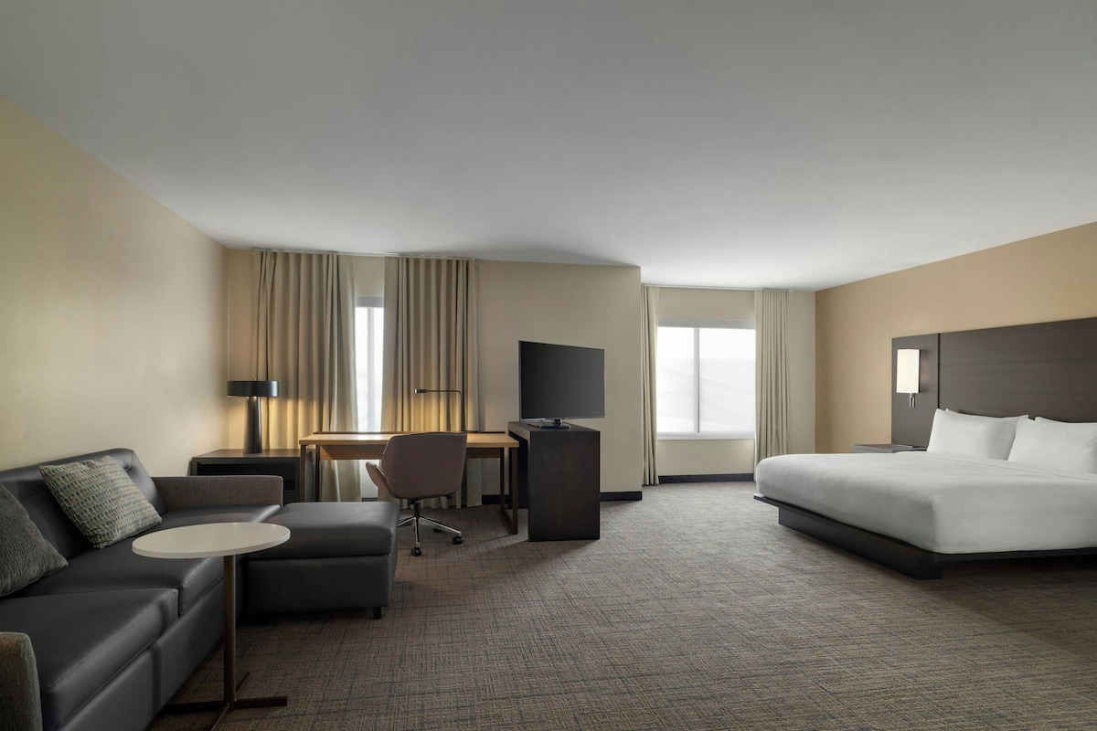 A hotel room with a bed, a desk, a chair, a sofa, and a television.