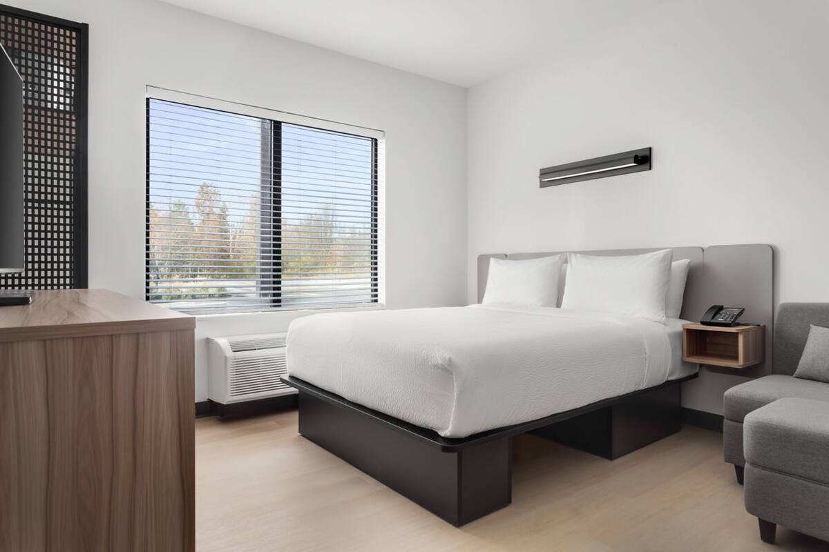 Un dormitorio moderno con cama, mesita de noche y un pequeño escritorio.