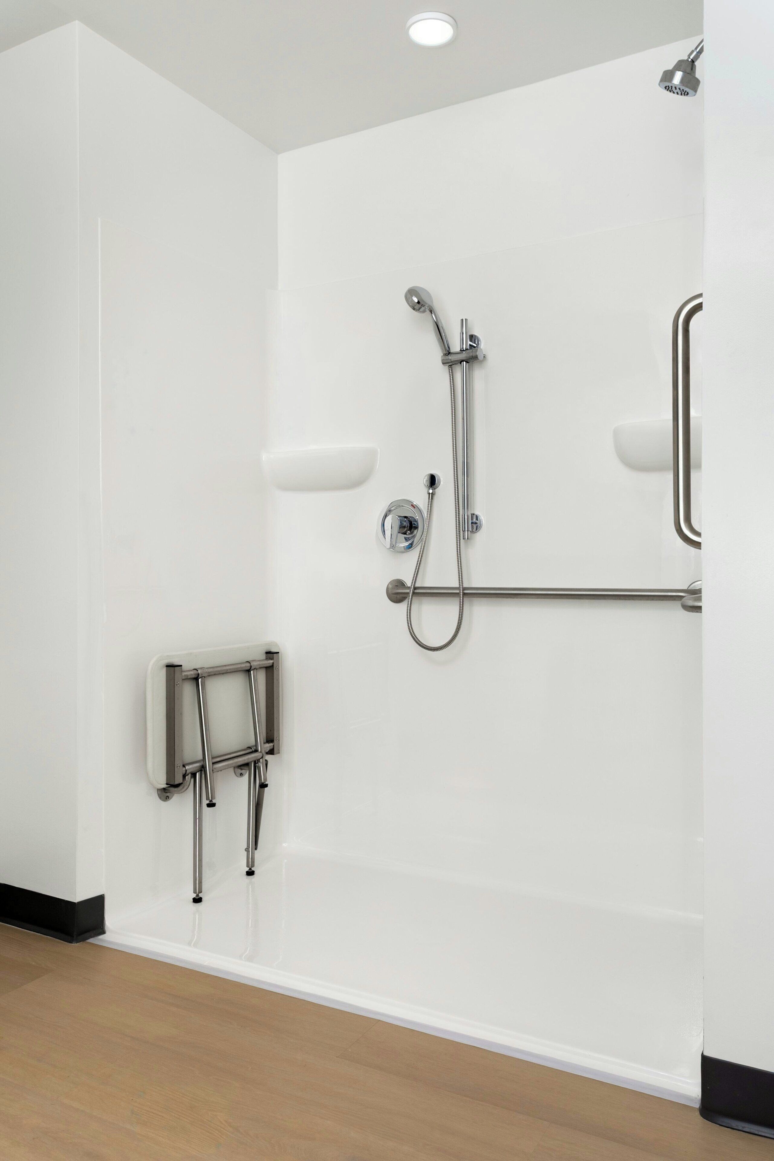 A modern bathroom with a shower, grab bars, and a handrail.
