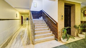A marble-floored hallway leading to a staircase with a wooden handrail and a door with a metal gate. - Classic Hotel sai Leela Residency (Ramagundam)