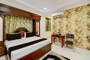 A hotel room with a large bed, a wooden headboard, a small table, a chair, and an air conditioning unit.