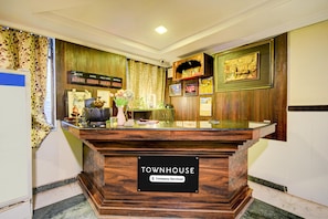A reception desk labeled 'TOWNHOUSE' with a 'Company-Serviced' sign, a digital clock, and a decorative wall with framed pictures and a clock.