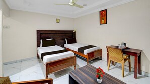 A hotel room with two single beds, a wooden desk, a chair, a ceiling fan, and a small table with a vase of flowers. - Classic Hotel sai Leela Residency (Ramagundam)