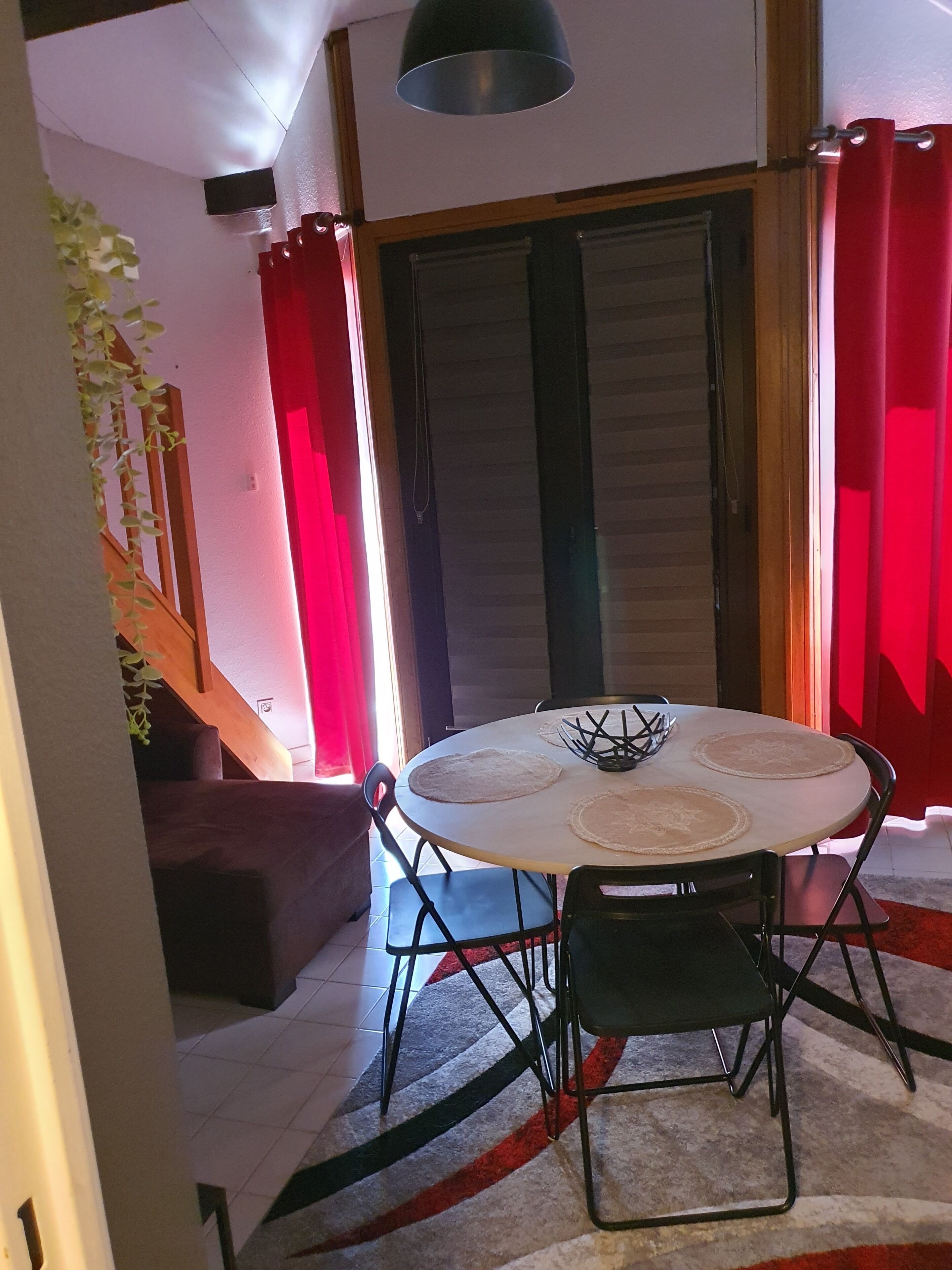 A dining area with a round table, black chairs, and a red curtain.