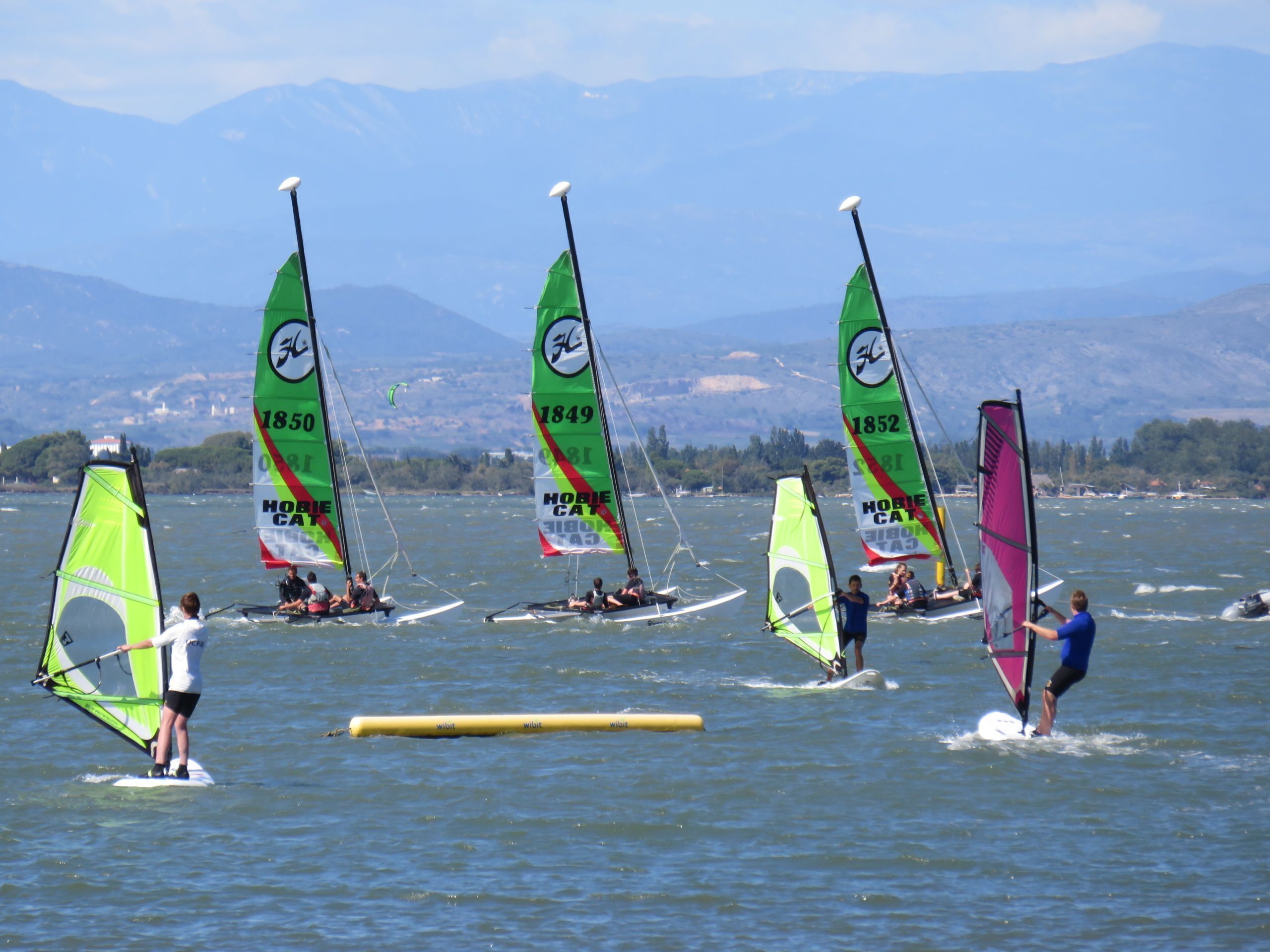 A group of people windsurfing on a lake with mountains in the background.