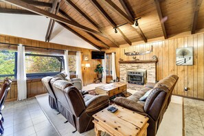 A cozy cabin interior with wooden walls, a fireplace, leather seating, and a television. - Ruby Retreat – Mountain Views, 2 Decks, Fire Pit, Creek, Fast WiFi, Generator (Franklin)