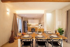A dining area with a wooden table set for four, surrounded by black chairs. A kitchen is visible in the background with modern appliances.