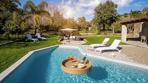 Piscina com espreguiçadeiras e suporte para bebidas, cercada por gramado e árvores.