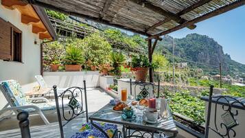A terrace with a table set for breakfast, outdoor seating, and a view of a mountainous landscape.