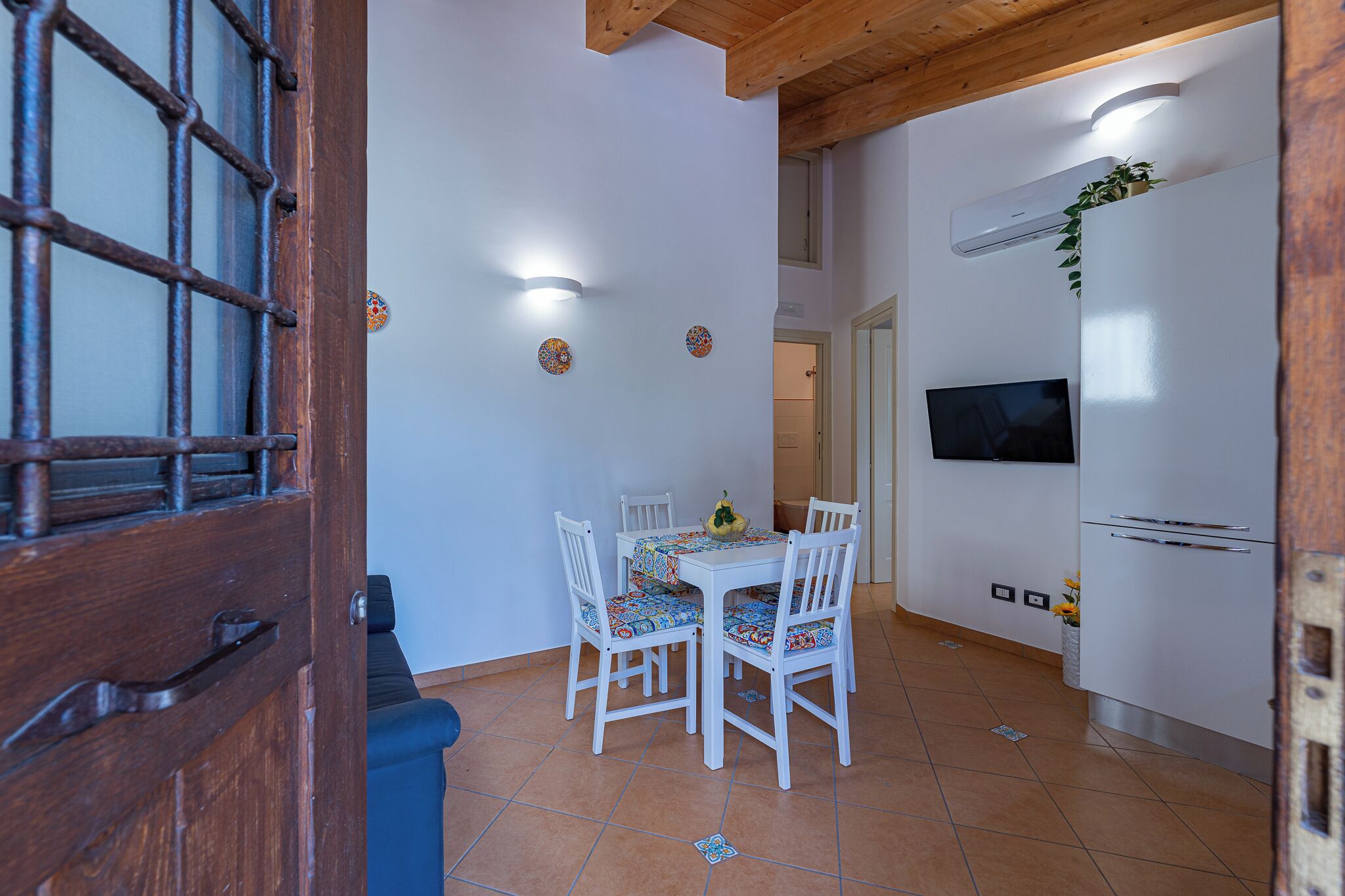 A dining area with a table and chairs, a TV mounted on the wall, and an air conditioning unit.