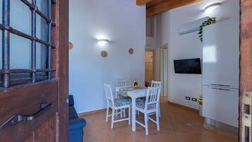 A dining area with a table and chairs, a TV mounted on the wall, and an air conditioning unit.
